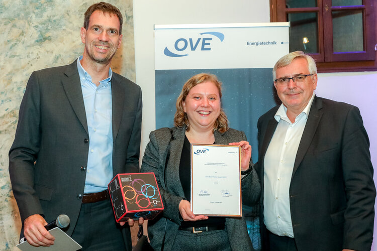 Weibliche Preisträgerin mit Urkunde und flankiert von zwei Männern